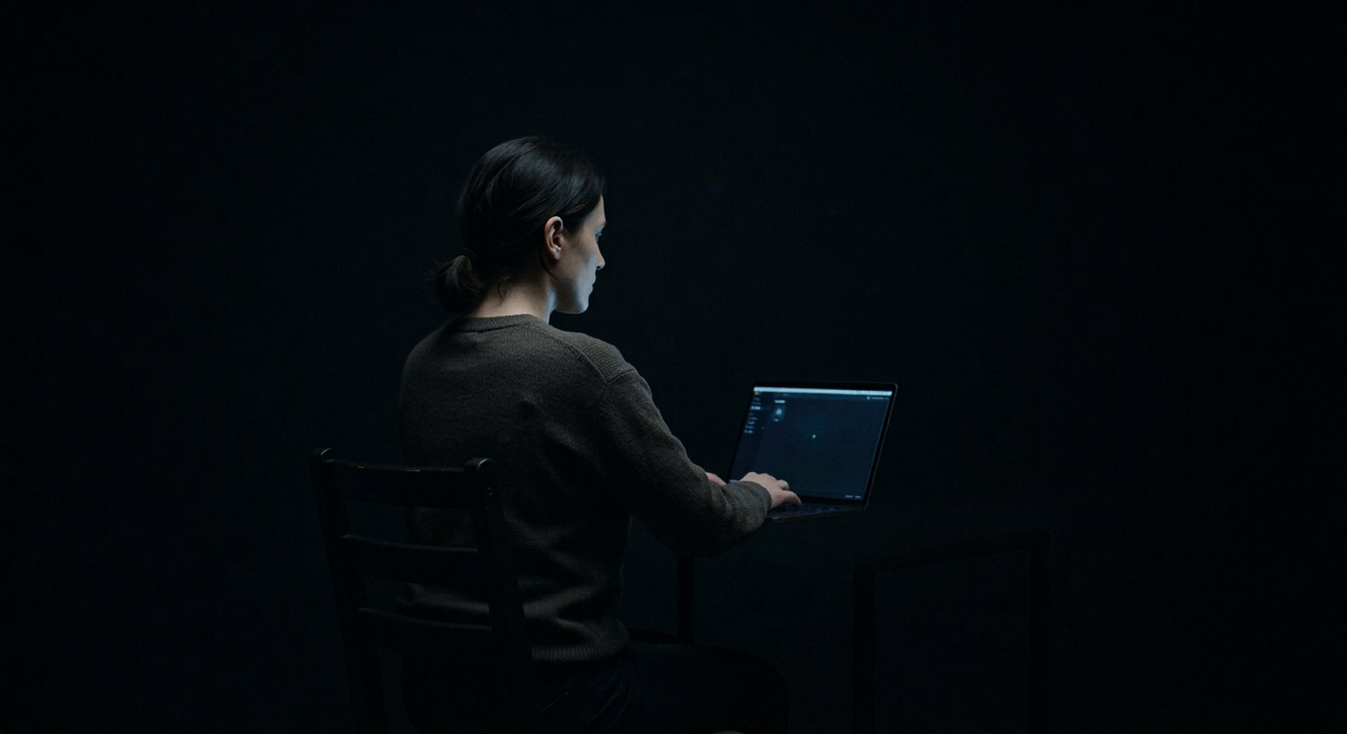Silhouette humaine assise dans la pénombre, lumière douce sur le visage, aucune identité reconnaissable